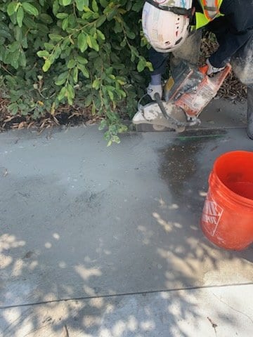TSIAC crew member in a hard hat saw-cutting a concrete slab beside a bucket of water