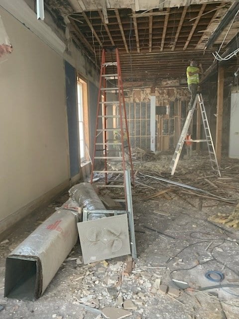 Interior gutted to the ceiling joists, with ladders, ductwork and debris on the floor