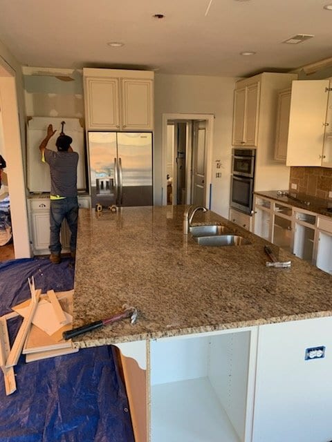 Crew member removing kitchen cabinets above a granite island, floor covered in tarps