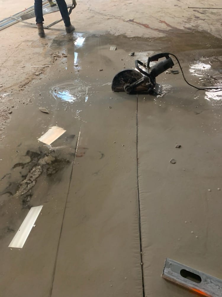 Hand-held concrete saw resting on a wet slab beside freshly cut joint lines