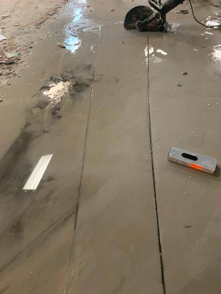 Concrete slab with straight saw-cut lines and a cut-off saw at the far end