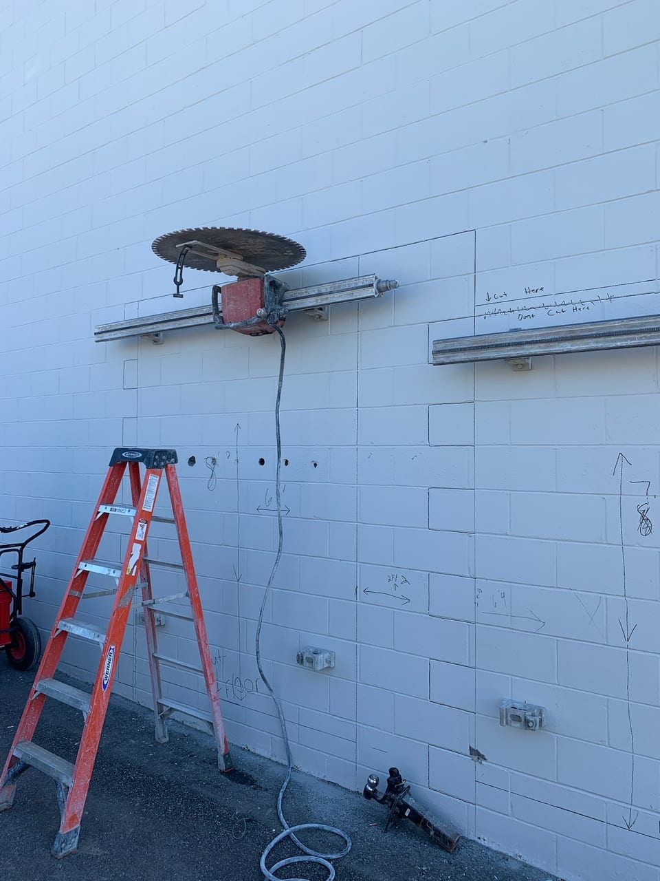 Track-mounted wall saw set up to cut an opening in a painted block wall, with a ladder alongside